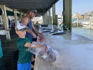 A young boy assists with fish preparation at a cleaning station on the dock, showcasing a variety of fish laid out for processing.