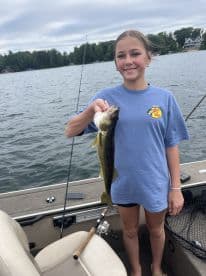 A young angler proudly displaying a Walleye while fishing on a boat, surrounded by a scenic lake environment.