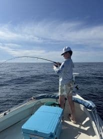 A young angler is actively reeling in a fish while fishing on a small boat in open waters, showcasing the excitement of the catch.
