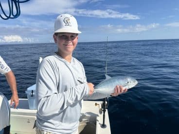 A young angler proudly displaying a caught fish while fishing on a boat in open waters.