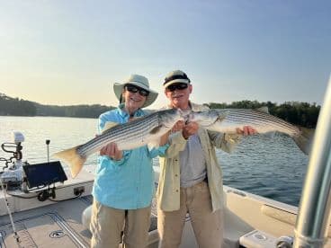 Two anglers proudly displaying their catch of striped bass while enjoying a serene morning on the lake.