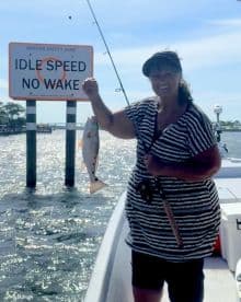 An angler proudly displaying a freshly caught Redfish while fishing in a scenic waterway, with a 'No Wake' sign in the background.