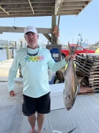 An angler proudly displaying a large Amberjack at the dock, showcasing a successful fishing trip.