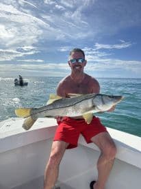 An angler proudly displaying a large Snook while fishing on a sunny day in open waters.