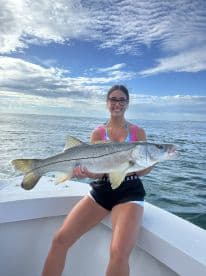A young angler proudly displaying a large Snook while aboard a boat, with a scenic ocean backdrop.