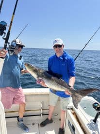 Two anglers proudly displaying a large Cobia aboard a fishing charter in open waters.