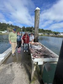 A group of four anglers proudly displaying their catch of various fish on a cleaning table at the dock, showcasing a successful fishing trip.