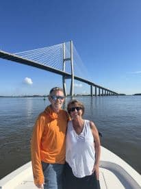 A couple enjoying a sunny day on their boat with a scenic bridge in the background, perfect for a relaxing fishing trip.
