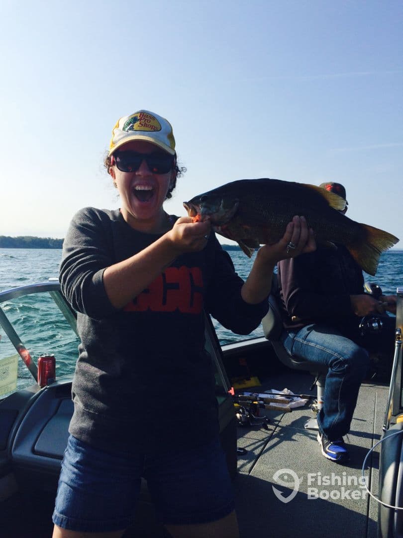 An excited angler proudly displaying a large Largemouth Bass while fishing on a boat, showcasing a vibrant day on the water.