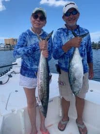 Two anglers proudly displaying their catches of King Mackerel aboard a fishing boat, enjoying a sunny day on the water.