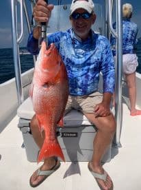 An angler proudly displaying a large Red Snapper while fishing on a boat in open waters.