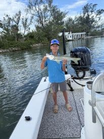 Young angler proudly holding a Snook while fishing from a boat in a scenic waterway.