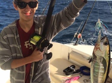 A young angler proudly displaying a caught fish while fishing on a boat, showcasing a vibrant ocean backdrop.