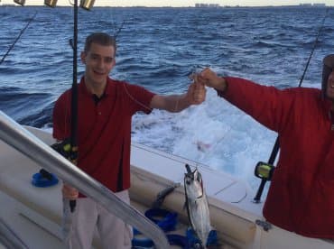 A young angler proudly displaying a caught fish while fishing on a charter boat, with a scenic ocean backdrop.