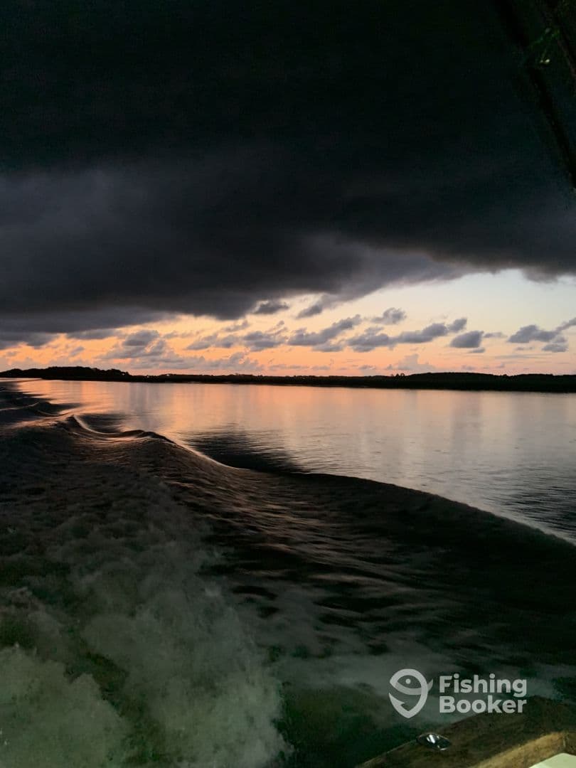 A scenic view of the water at dusk, showcasing the reflection of clouds and the fading light, with the boat's wake visible.