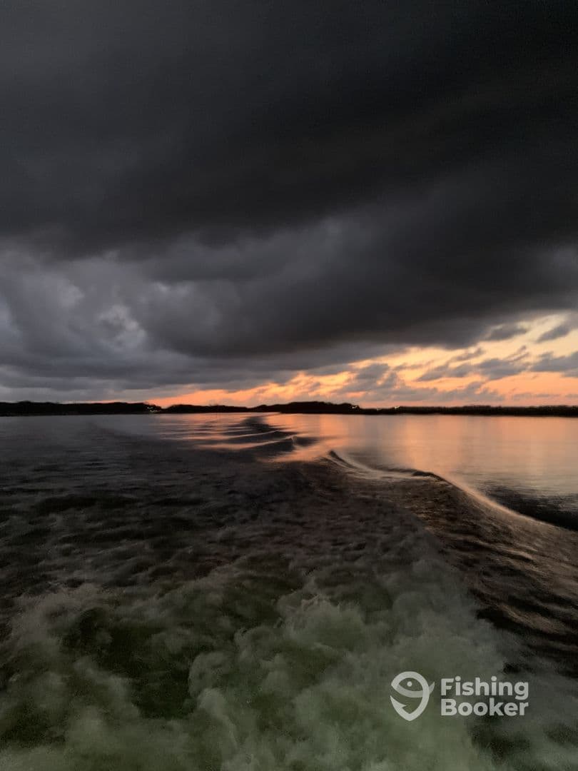 A scenic view of a darkening sky over calm waters, capturing the wake of a boat during sunset.