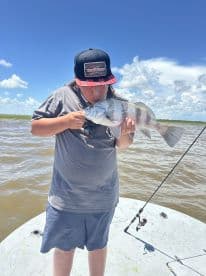 A young angler joyfully holding a large fish while fishing on a sunny day, showcasing a memorable catch in a scenic waterway.