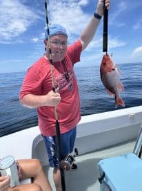 An angler proudly displaying a Red Snapper while fishing on a sunny day in open waters.