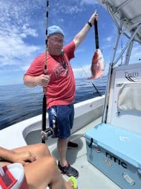 An angler proudly displaying a Red Snapper while fishing on a catamaran in open waters.