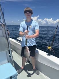 A young angler proudly displaying a Snapper caught while fishing on a boat in clear blue waters.