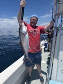 An angler proudly displaying a large fish while fishing on a boat in open waters, showcasing a successful day on the Gulf Coast.