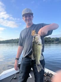 A young angler proudly displaying a large Largemouth Bass while fishing on a serene lake.