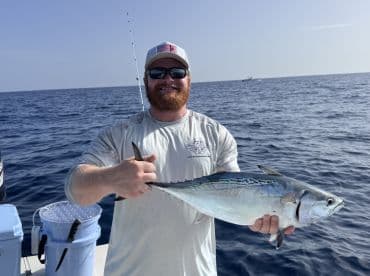 An angler proudly displaying a freshly caught Bonito while fishing offshore, showcasing the vibrant blue waters of the ocean.