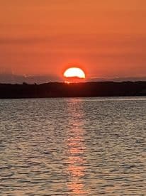 A stunning sunset over calm waters, reflecting vibrant orange hues, creating a serene atmosphere ideal for fishing adventures.