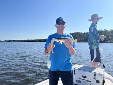 An angler proudly displaying a speckled trout while fishing on a sunny day in a freshwater lake.