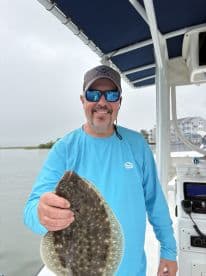 Angler proudly displaying a Flounder while aboard a fishing boat, showcasing a successful day on the water.