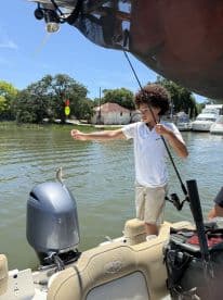 A young angler is reeling in a small fish while fishing from a boat in a calm waterway, showcasing an engaging fishing experience.