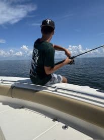 A young angler casting a line from the bow of a boat on a sunny day, enjoying a fishing adventure in open waters.