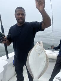Angler proudly displaying a large Flounder while fishing on a boat in foggy conditions.