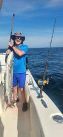 Angler proudly displaying a large Barracuda while fishing on a boat in open waters.
