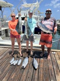 Three anglers proudly displaying their catch of Mahi Mahi and Bonito on the dock after a successful fishing trip.