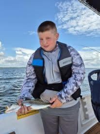 A young angler proudly displaying a Speckled Trout while fishing on a boat, showcasing a beautiful day on the water.