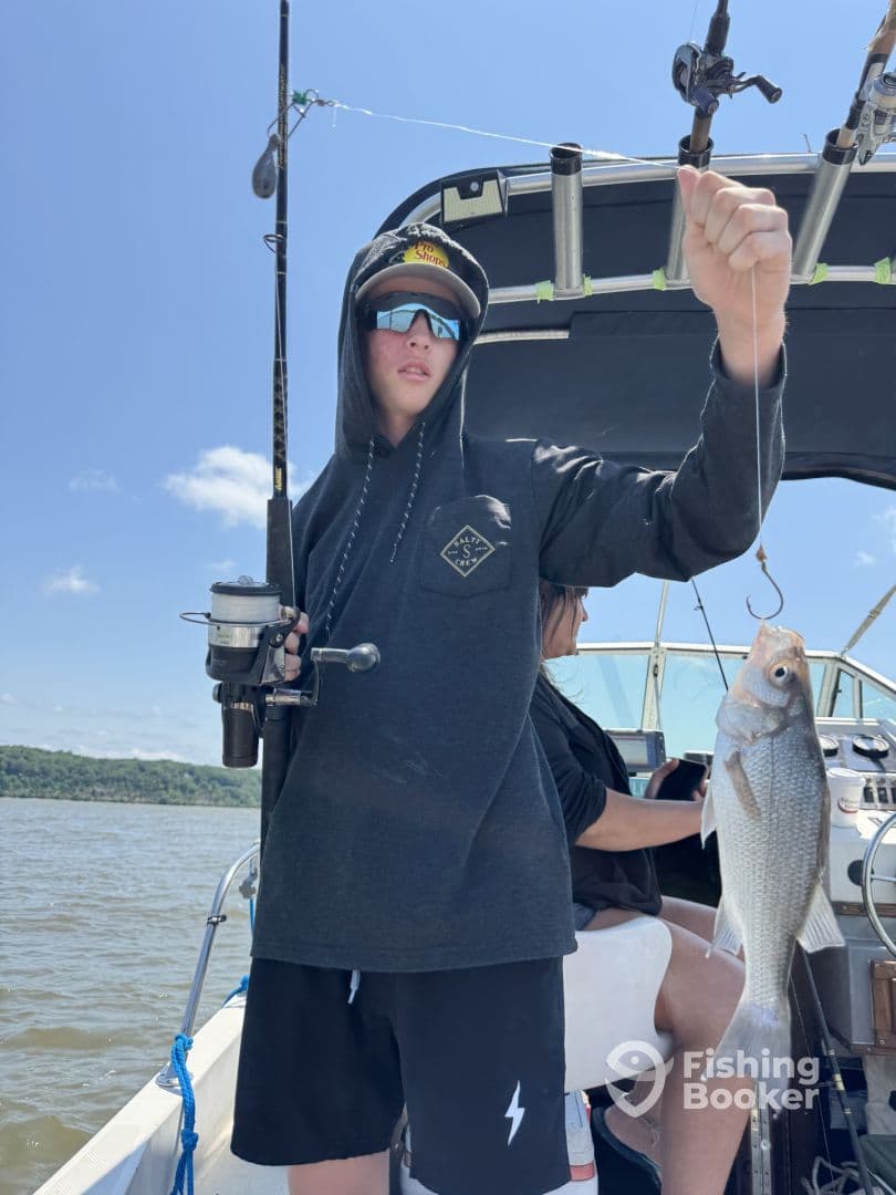 A young angler proudly displaying a freshly caught fish while fishing on a boat, enjoying a sunny day on the water.