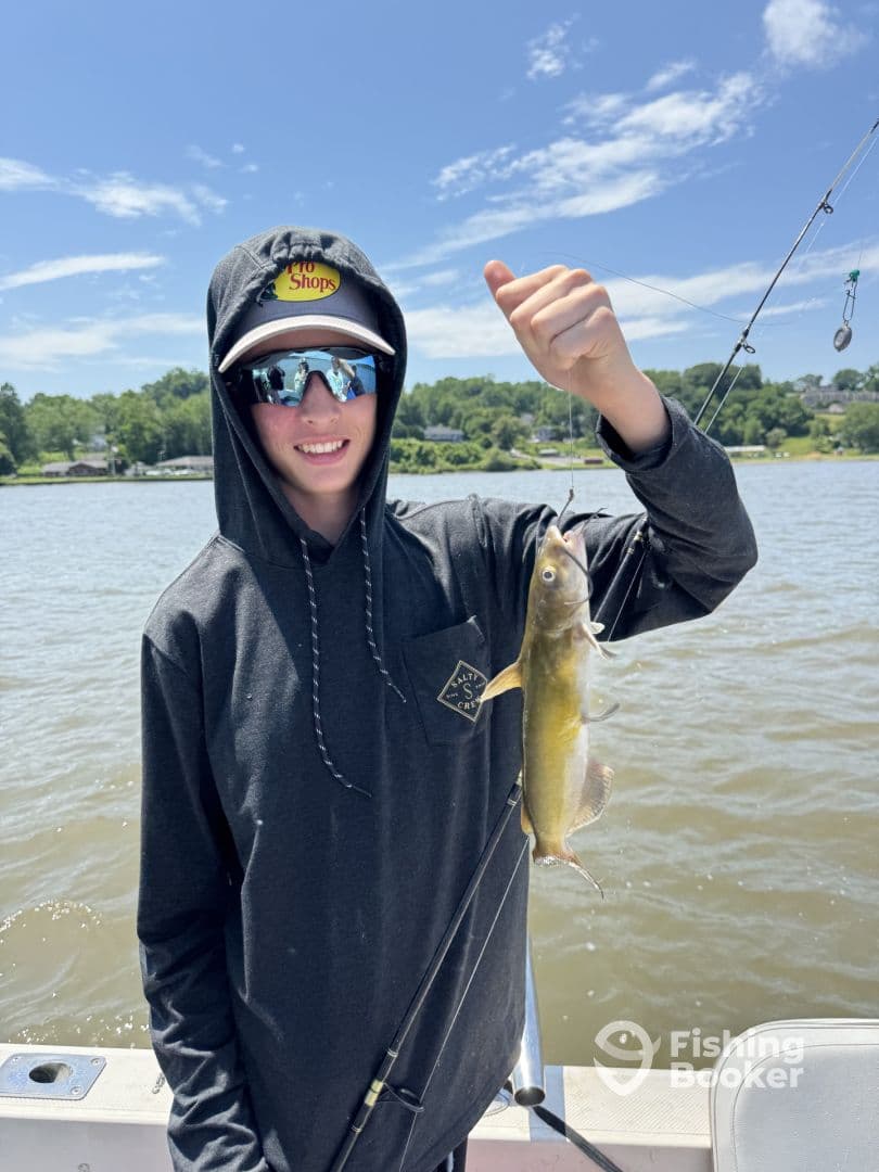 A young angler proudly displaying a catfish while fishing on a sunny day, showcasing the excitement of a successful catch.