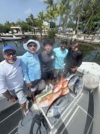 Group of anglers proudly displaying a variety of fish, including Mahi Mahi and Snapper, aboard a boat in a tropical setting.