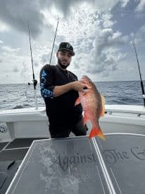Angler proudly displaying a vibrant Red Snapper while fishing offshore, showcasing a successful day on the water.