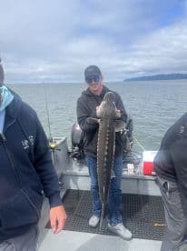 Angler proudly displaying a large Sturgeon on a fishing boat, showcasing a successful catch during a coastal fishing trip.