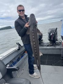An angler proudly displaying a large Sturgeon while fishing on a boat in a scenic waterway.