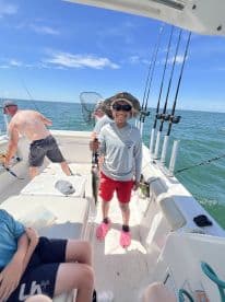 A young angler proudly displaying a caught fish aboard a fishing boat, enjoying a sunny day on the water.