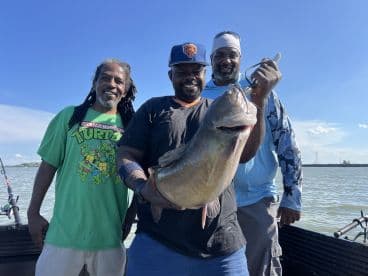 Three anglers proudly displaying a large catfish while fishing on a boat, showcasing a successful day on the water.