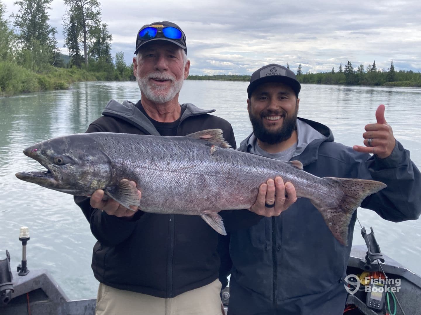 Two anglers proudly displaying a large Chinook Salmon while fishing on a scenic river.