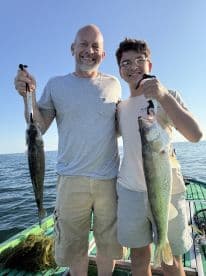 A proud father and son duo displaying their catch of Walleye while fishing on a sunny day.