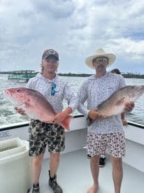 Two anglers proudly displaying their large Red Snapper on a fishing charter in a coastal environment.
