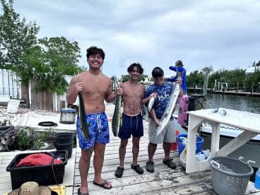 Two young anglers and an adult proudly displaying their catch of Mahi Mahi and Barracuda at the dock after a successful fishing trip.