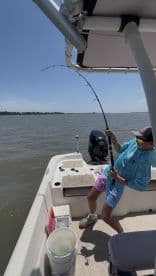 A young angler is reeling in a catch while fishing from a boat on a sunny day, showcasing the excitement of the fishing experience.