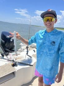 A young angler proudly displaying a small shark while fishing on a boat in a coastal waterway.